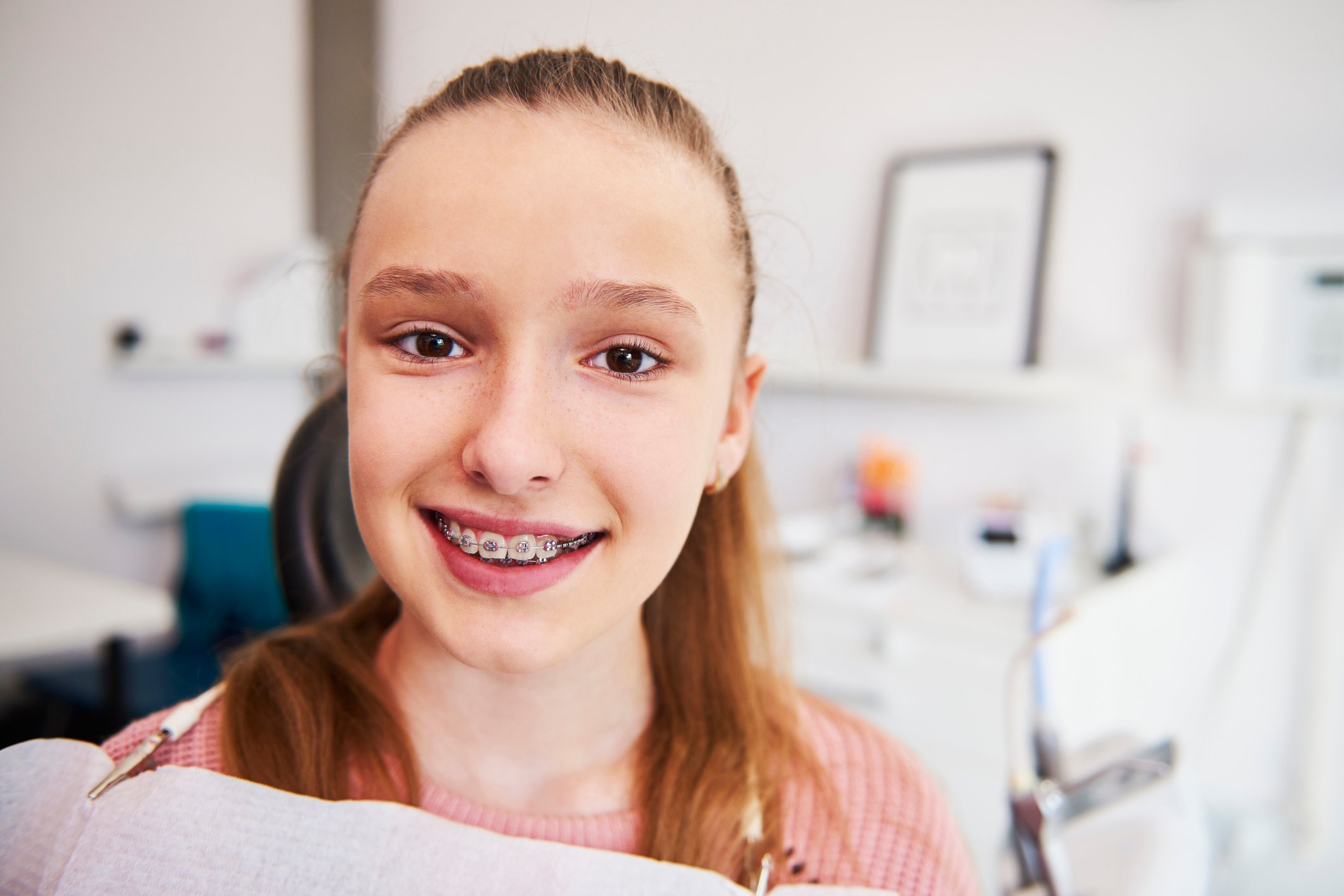 Mädchen mit Zahnspange sitzt auf dem Behandlungsstuhl eines Zahnarztes und lächelt in die Kamera