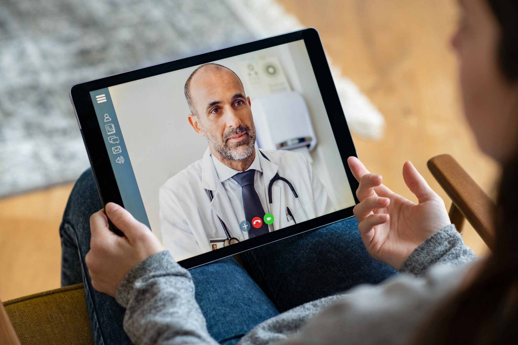 Bild eines Patienten, der ein iPad auf dem Schoß hält und per Videosprechstunde mit einem Arzt kommuniziert