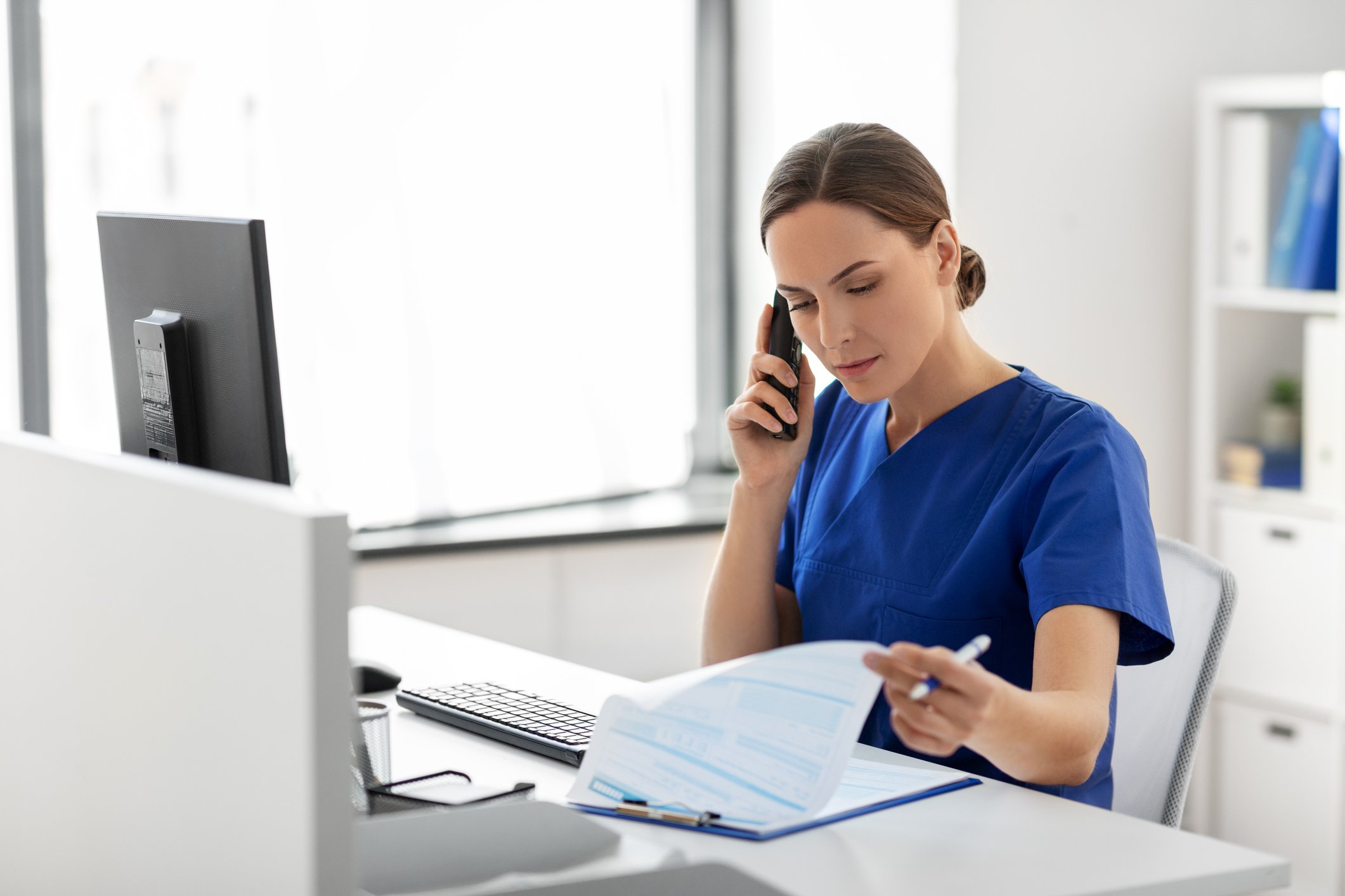 Eine medizinische Fachangestellte sitzt an der Rezeption und telefoniert
