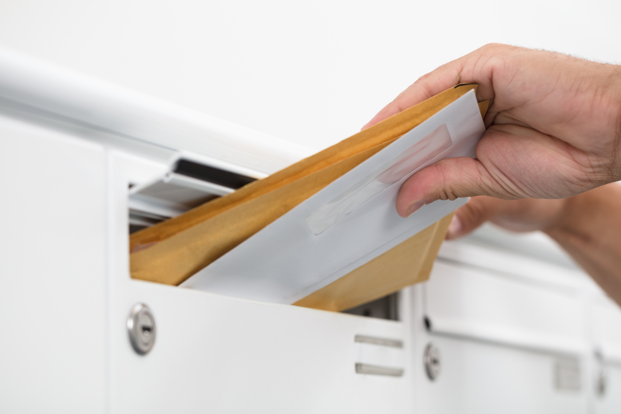 Eine Hand wirft mehrere Briefe in einen Briefkasten ein