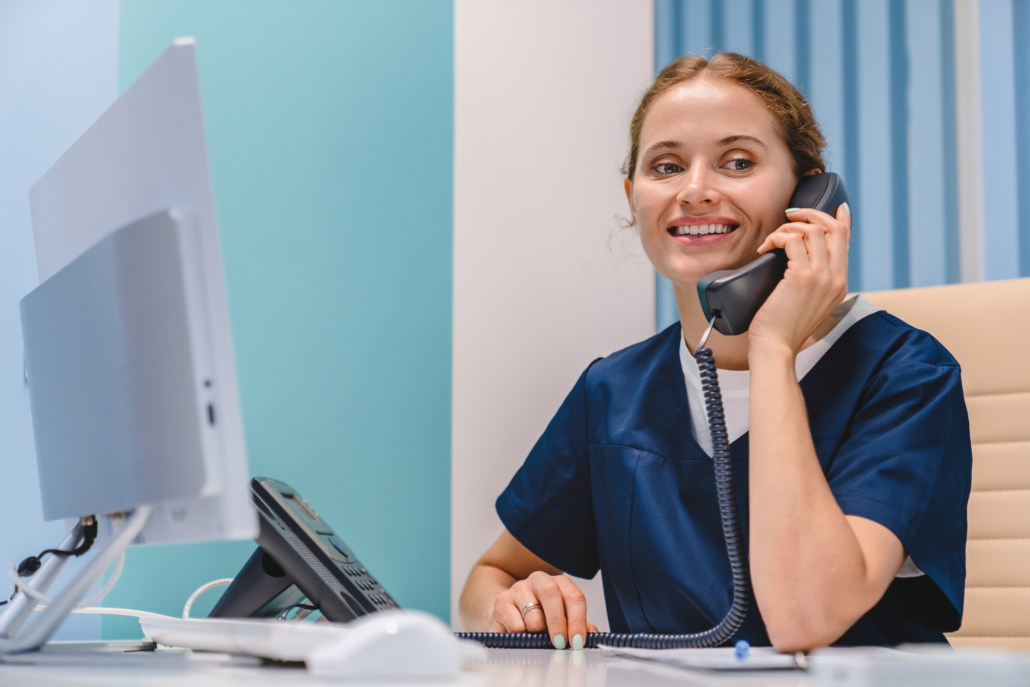 Medizinische Fachangestellte sitzt lächelnd am Schreibtisch und telefoniert – Titelbild des jameda Blogposts zum Thema digitale Praxis